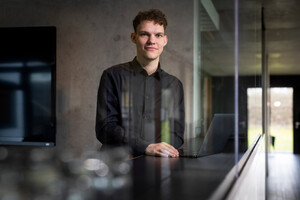 Ein junger Mann steht im Verwaltungsgebäude der MATTHÄUS SCHMID Gruppe und lächelt in die Kamera. Er studiert in Biberach und absolviert bei Schmid ein Praktikum.