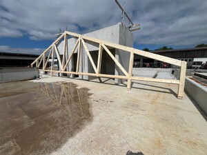 Das Bild zeigt eine Holz-Hybridbau-Baustellensituation in Aulendorf. Ein Dachbinder steht auf der Bodenplatte und lehnt an einem Rohbauteil aus Beton.