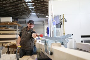 Das Bild zeigt einen Holzbau-Facharbeiter, der eine vollautomatische Abbundanlage bedient.
