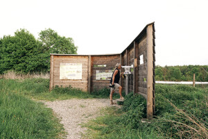 Auf dem bild sieht man einen SIchtschutz aus Holz, ein Mann schaut durch das Fernrohr.