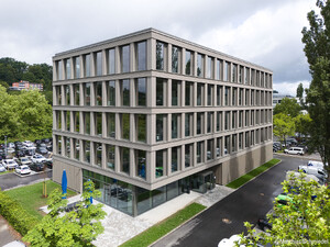 Auf dem Bild sieht man ein Bürogebäude umgeben von kleinen Grünflächen und Parkplätzen