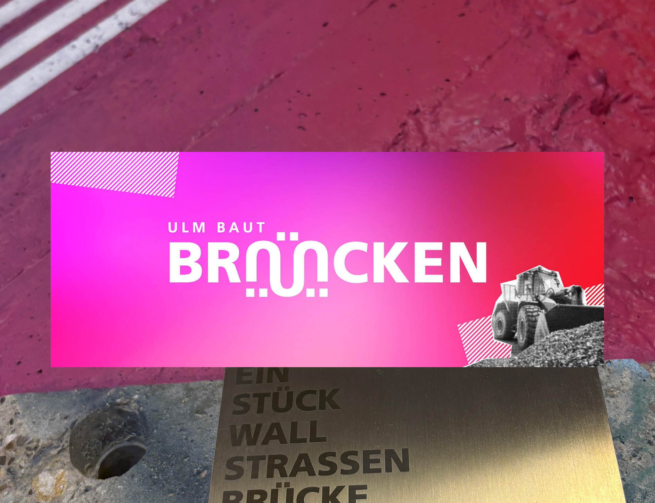 Das Foto zeigt das Visuall der Ausstellung "Ulm baut Br&uuml;cken". Vor einem pinken Hintergrund steht ""lm baut Br&uuml;cken". Das &Uuml; im Wort Br&uuml;cken ist wie eine Br&uuml;cke gebaut.
