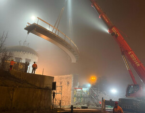 Das Bild zeigt, wie der Schwerlastenkran die Brücke über den Brücken-Widerlager einpasst.