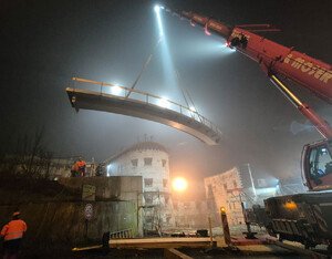 Das Bild zeigt, wie der Schwerlastenkran die Brücke über den Brücken-Widerlager einpasst.