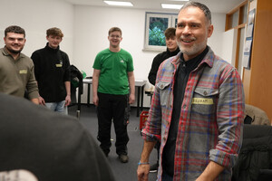 Das Bild zeigt junge Auszubildende, die in einem Kreis stehen. Ein Referent lächelt einem Teilnehmer auffördernd zu