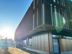 Die Abbildung zeigt eine Ansicht auf das Feuerwehrhaus der Stadt Weißenhorn. Man sieht im oberen Bereich die Fassade aus senkrechten Stahlteilen. Diese sind rostfarben. Im unteren Teil besteht die Fassade aus Holz.