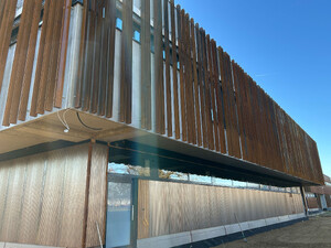 Die Abbildung zeigt eine Ansicht auf das Feuerwehrhaus der Stadt Weißenhorn. Man sieht im oberen Bereich die Fassade aus senkrechten Stahlteilen. Diese sind rostfarben. Im unteren Teil besteht die Fassade aus Holz.