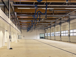 Die Abbildung zeigt eine große Halle. Rechts sind Tore zu sehen. Von der Decke hängen Versorgungsleitungen