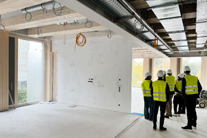 Das Foto zeigt eine Besuchergruppe in Sicherheitswesten und Bauhelmen, die sich die Baustelle von innen anschauen. Man sieht die Holzkonstruktion des Innenraumes.