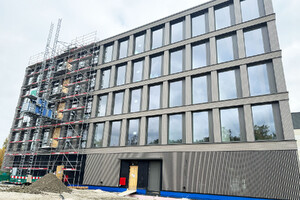 Das Foto zeigt die Front eines sich im Bau befindlichen fünfstöckigen Bürogebäudes. Ein Teil der Fassade ist angerüstet.