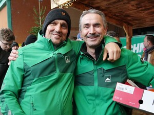 Das Foto zeigt zwei Schmid Mitarbeitende, die sich auf dem Schmid Weihnachtsbaum freundschaftlich umarmen.