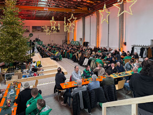 Das Foto zeigt eine weihnachtlich geschmückte Halle, mit einem großen Weihnachtsbaum und vielen Schmid Mitarbeitenden