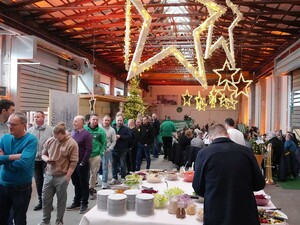Das Foto zeigt Schmid Mitarbeitende, die vor dem Buffet in der Reihe stehen. Von der Decke hängen beleuchtete Stern.