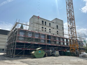 Das Foto zeigt eine Baustelle in Aktion. Es wird ein Hybridprojekt realisiert. Der Massivbaukern sowie eine Teilmontage der Stockwerke aus Holzelementen ist zu sehen.