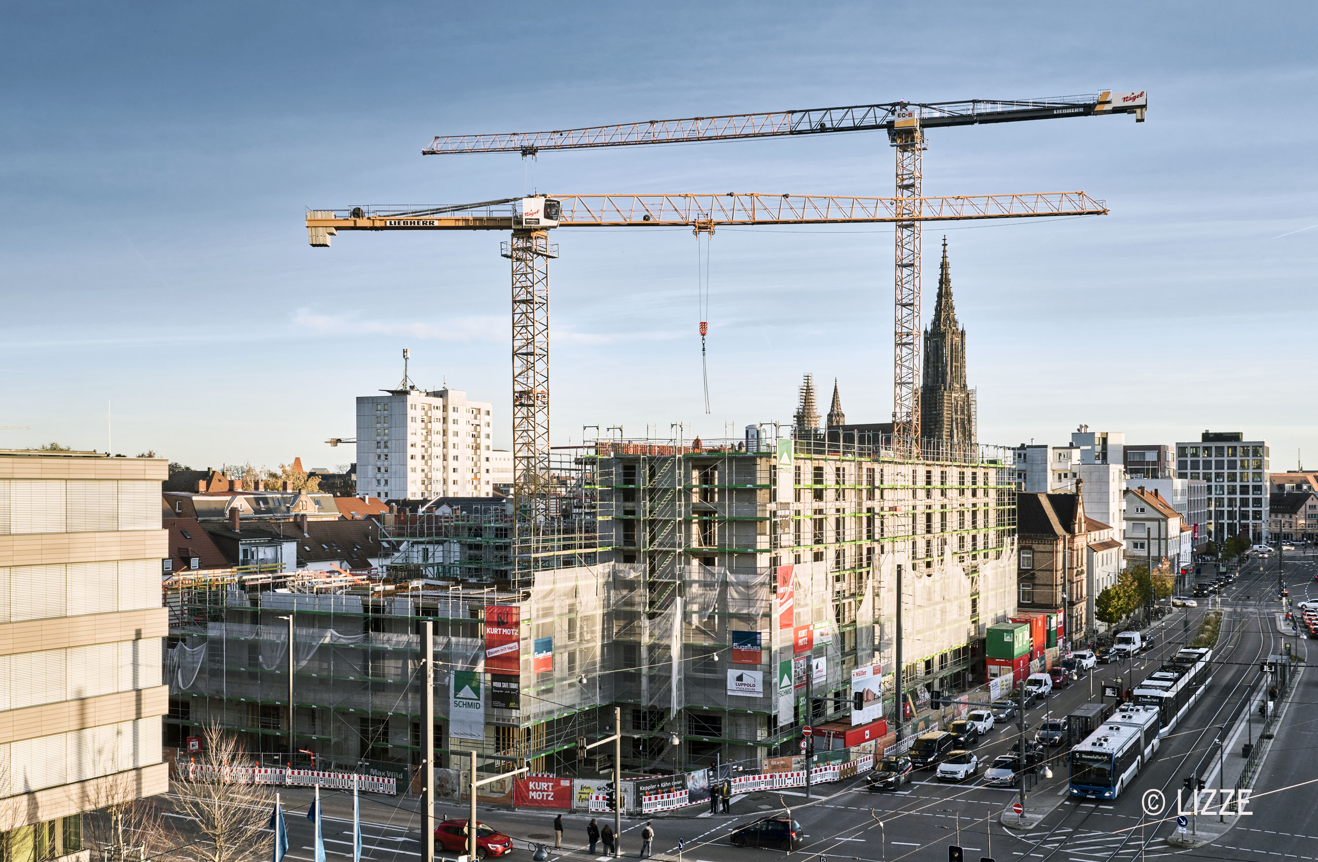 Auf dem Foto ist eine gro&szlig;e Baustelle und 2 Krane zu sehen. Im Hintergrund ist das Ulmer M&uuml;nster zu sehen. Die Baustelle ist im Rohbauzustand und das bestehende Geb&auml;ude einger&uuml;stet