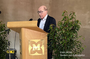 Auf dem Foto ist Erwin Müller zu sehen. Er steht hinter einem Rednerpult. Auf dem Rednerpult ist das DM-Markt-Müllerlogo zu sehen