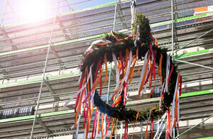 Auf dem Foto ist der Richtkranz zu sehen, der beim Richtfest des Wohn- und Geschäftshauses Müller am Kran hochgezogen wurde.