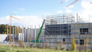 Das Foto zeigt eine Baustelle in der Rohbauphase. Zu sehen sind hohe Betonpfeiler, ein Rohbau, der eingerüstet ist und Krane