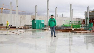 Das Foto zeigt einen Facharbeiter auf einer Baustelle. Im Hintergrund sind Betonpfeiler und eine Betonwand zu sehen.