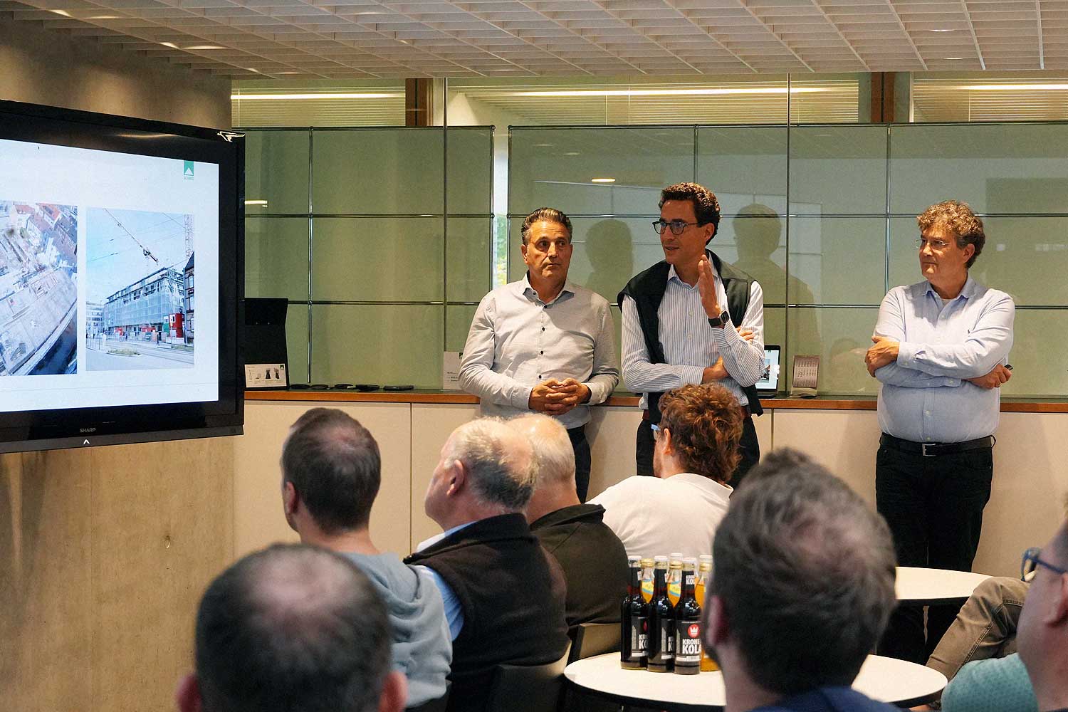 Das Foto zeigt sitzendes Publikum im Atrium des SCHMID Verwaltungsgebäudes. Das Publikum hört einen Vortrag der Geschäftsleiter, die seitlich an der Wand stehen. Es wird einen PPT-Präsentation abgespielt.