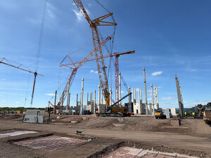 Raupenkran und Baukrane montieren Betonfertigteile für das neue Produktionsgebäude von Vetter in Saarlouis. Die Tragwerksstützen und erste Wandelemente des Rohbaus sind bereits errichtet.