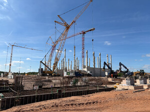 Baustelle des neuen Vetter-Produktionsgebäudes in Saarlouis mit Fundamentarbeiten im Vordergrund sowie Raupenkranen und montierten Betonstützen im Bereich des entstehenden Rohbaus.