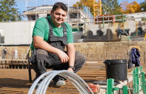 Das Foto zeigt einen Baufacharbeiter in Latzhose auf der Baustelle 